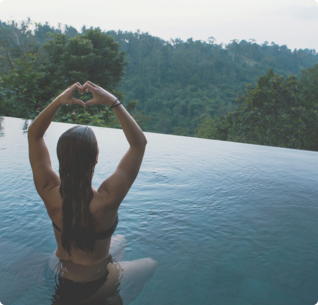 Woman in infinity pool overlooking a forest putting her hands up to signal a heart HBOT4LIFE makes you feel better